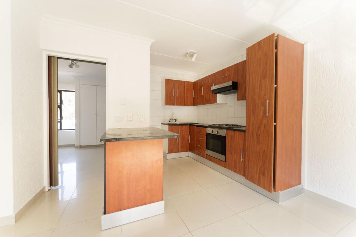 A clean, functional kitchen featuring wood-finish cabinetry, granite countertops, built-in oven, gas hob, and a breakfast nook, with neutral tiled flooring throughout.