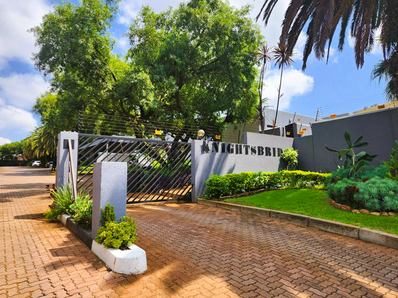 The secure entrance to the Knightsbridge complex features a paved driveway, automated security gate, electric fencing, and well-maintained landscaped garden beds.