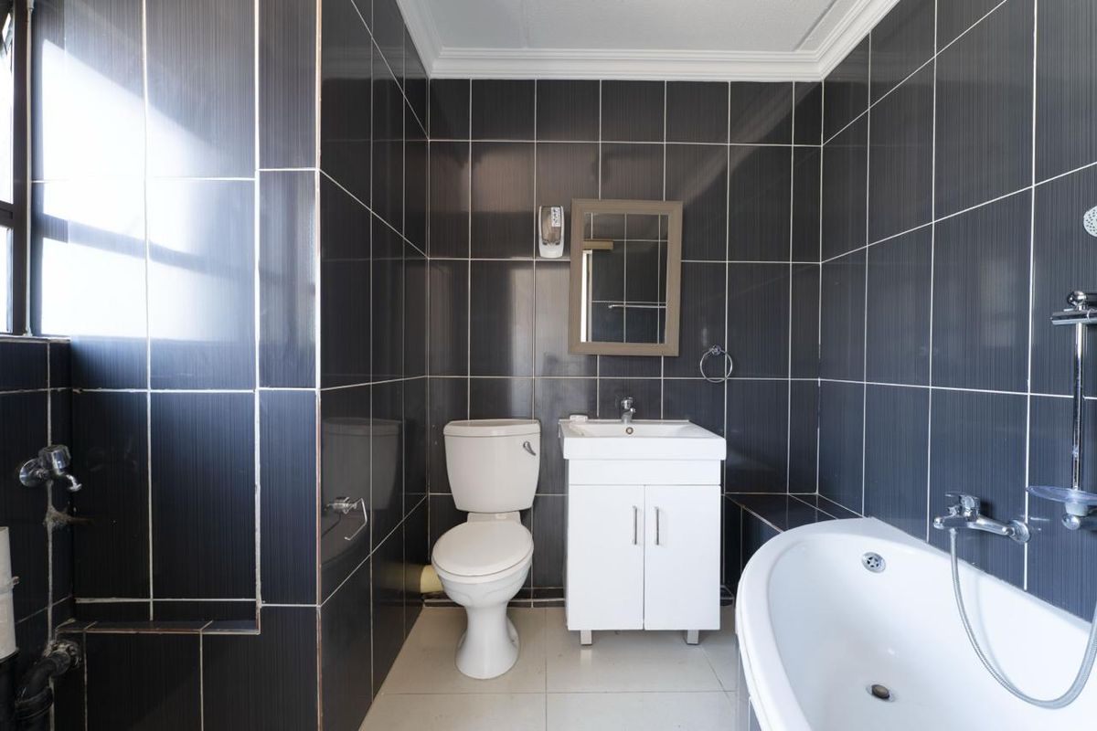 A compact bathroom featuring dark wall tiles, a white vanity with basin, a toilet, and a bathtub.
