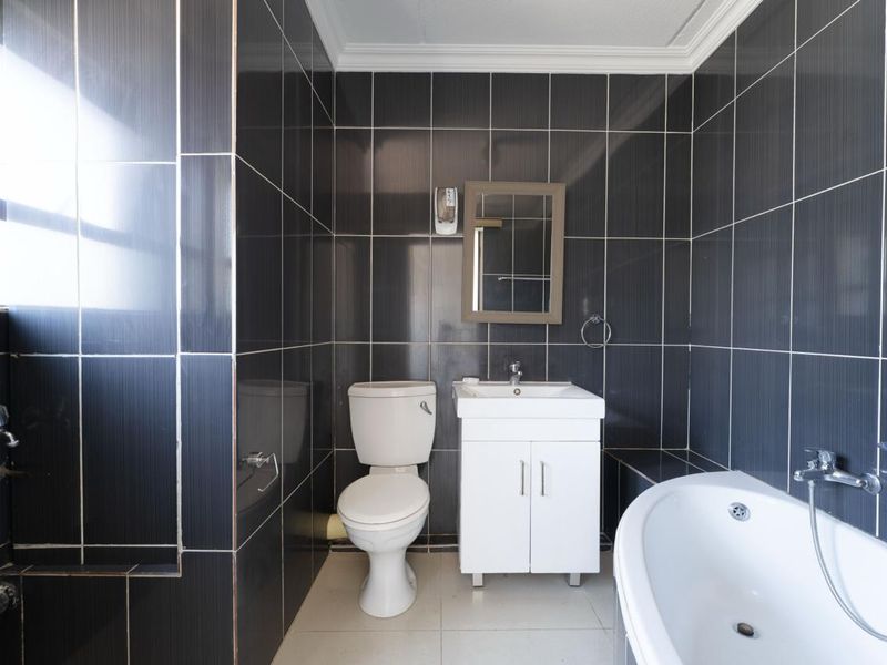 A compact bathroom featuring dark wall tiles, a white vanity with basin, a toilet, and a bathtub.