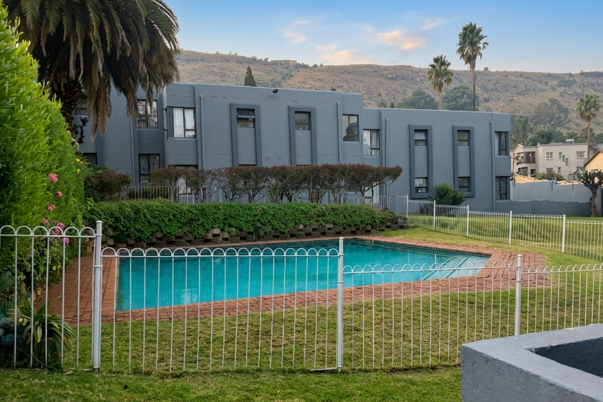 A well-maintained communal swimming pool area featuring brick coping, metal safety fencing, and landscaped garden surrounds set against a modern apartment building.