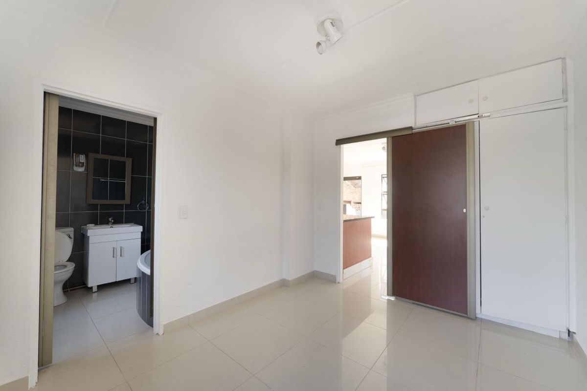 An empty bedroom featuring tiled flooring, built-in cupboards, and direct access to an en-suite bathroom.