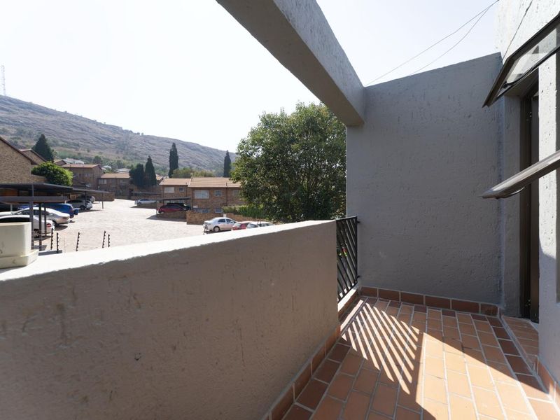 A private balcony featuring terracotta tiled flooring, a concrete balustrade, and metal railing, offering views over the apartment complex and surrounding landscape.