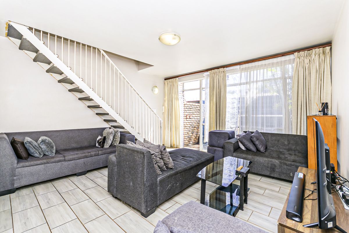 A living room featuring tiled flooring, a staircase with a metal balustrade, and access to an outdoor area through a sliding glass door.