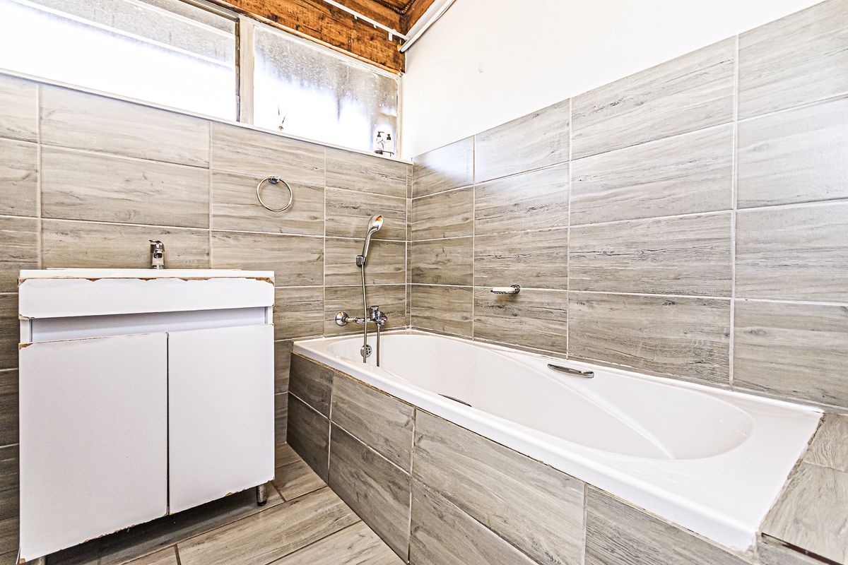 A functional bathroom featuring a built-in vanity, bathtub with handheld shower mixer, and neutral wood-look wall and floor tiling.