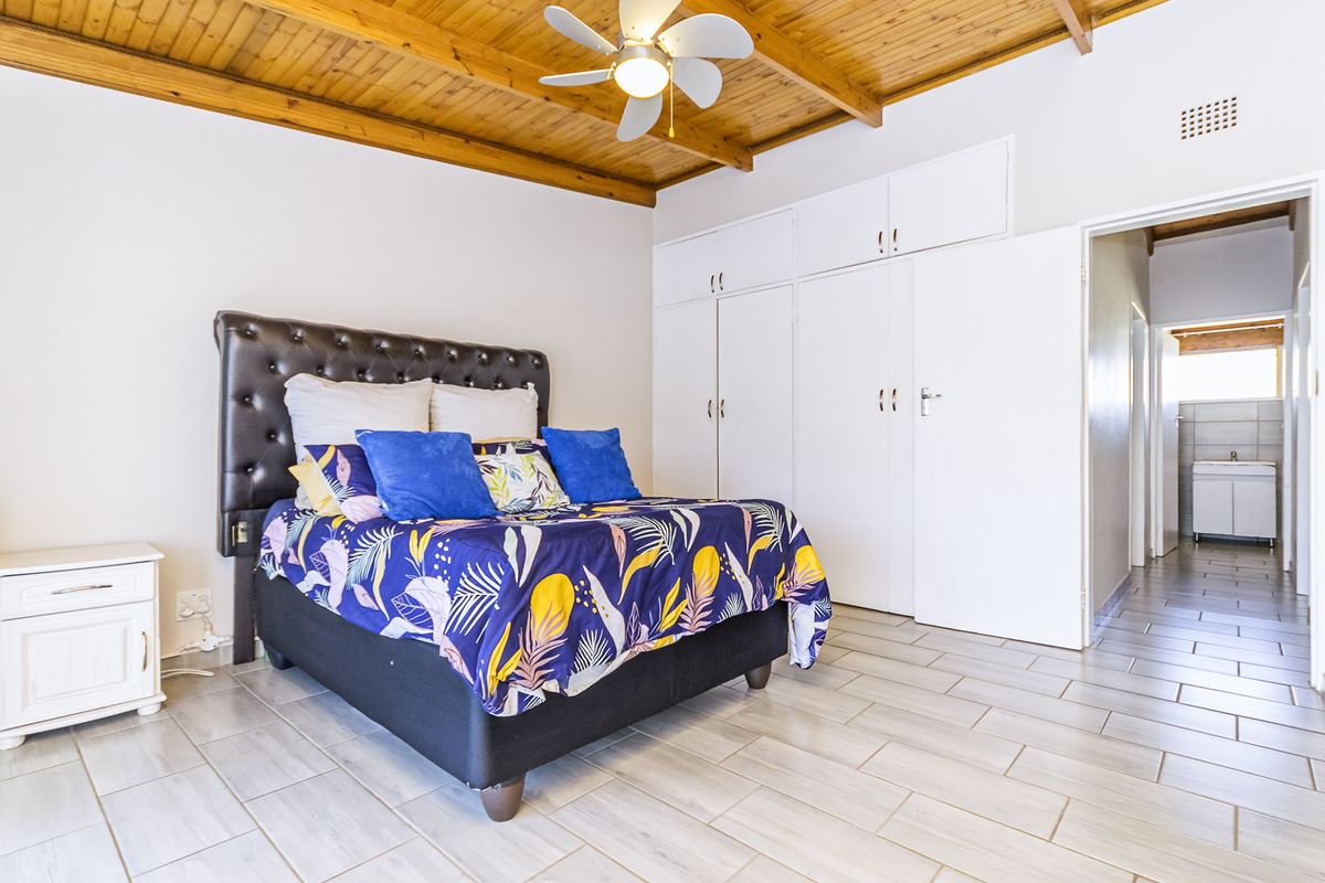 Spacious bedroom featuring a warm timber ceiling, ceiling fan, and extensive built-in cupboard storage, with direct access to an adjoining bathroom.