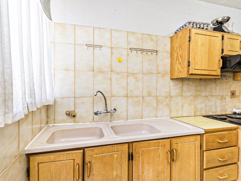 A dated kitchen area featuring wooden cabinetry, a double basin sink, and tiled backsplash with an integrated hob and extractor fan.