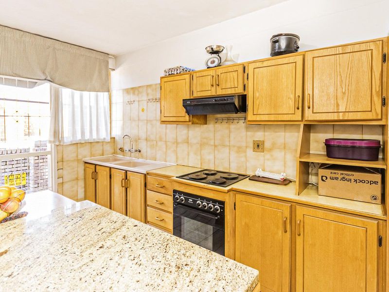 A functional kitchen featuring traditional wooden cabinetry, granite countertops, a built-in oven with hob, and a tiled backsplash with a double sink.