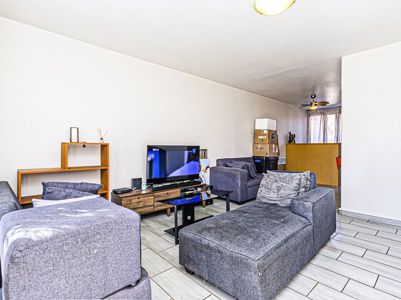 A living room area featuring light-colored tiled flooring and a ceiling fan, providing a functional space with direct access to the adjacent room.