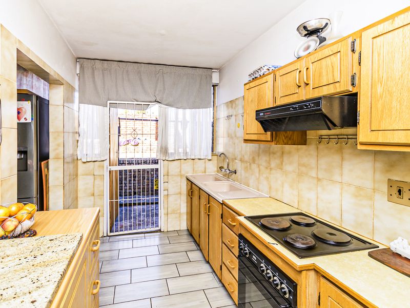 A functional kitchen featuring wooden cabinetry, built-in oven and hob, tiled splashbacks, and direct access to an exterior area via a security gate.
