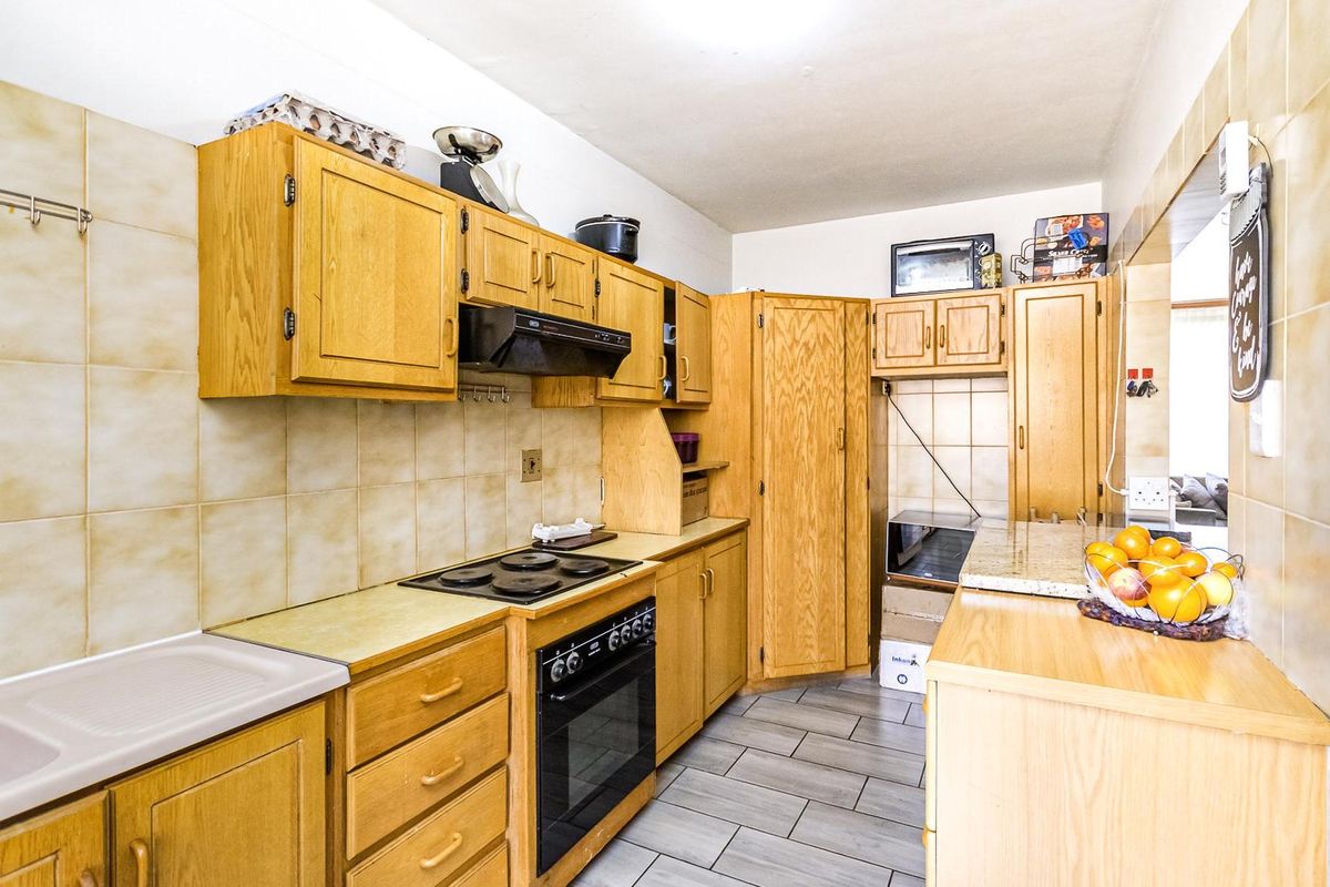 A functional kitchen featuring wooden cabinetry, a built-in oven with hob, extractor fan, and tiled flooring, offering a classic layout with ample storage space.