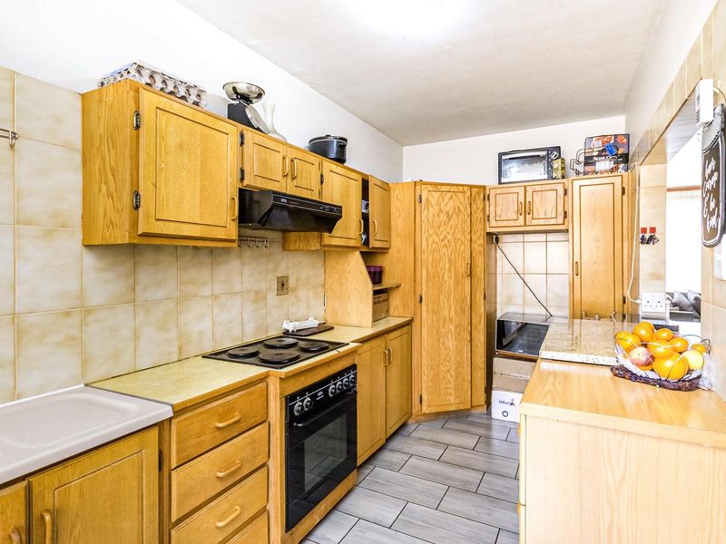 A functional kitchen featuring wooden cabinetry, a built-in oven with hob, extractor fan, and tiled flooring, offering a classic layout with ample storage space.