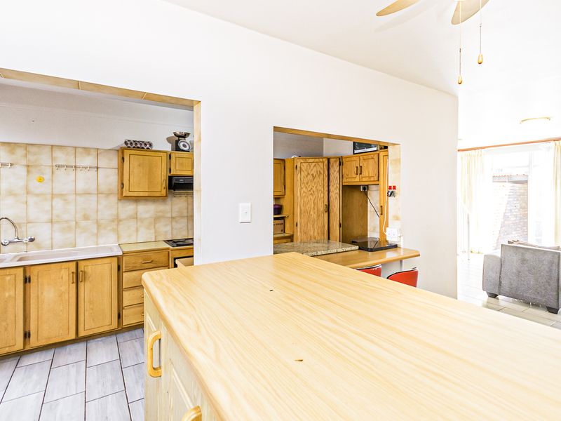 Open plan kitchen and living area featuring wooden cabinetry, a breakfast counter, and tiled flooring, offering a functional layout with potential for modern updates.