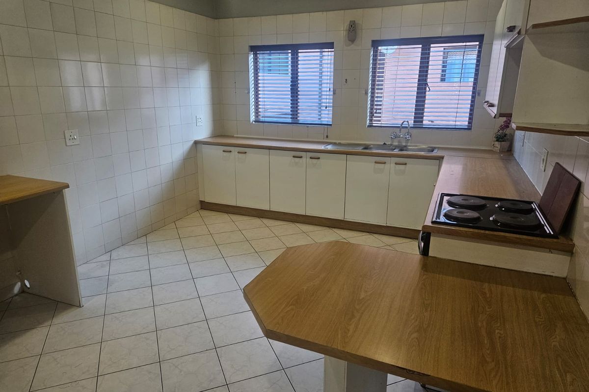 A functional, empty kitchen featuring laminate countertops, a built-in electric hob, double sink, and tiled finishes, offering a blank canvas for modern updates.