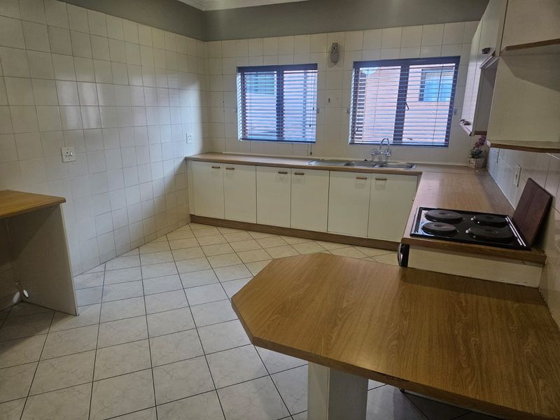 A functional, empty kitchen featuring laminate countertops, a built-in electric hob, double sink, and tiled finishes, offering a blank canvas for modern updates.