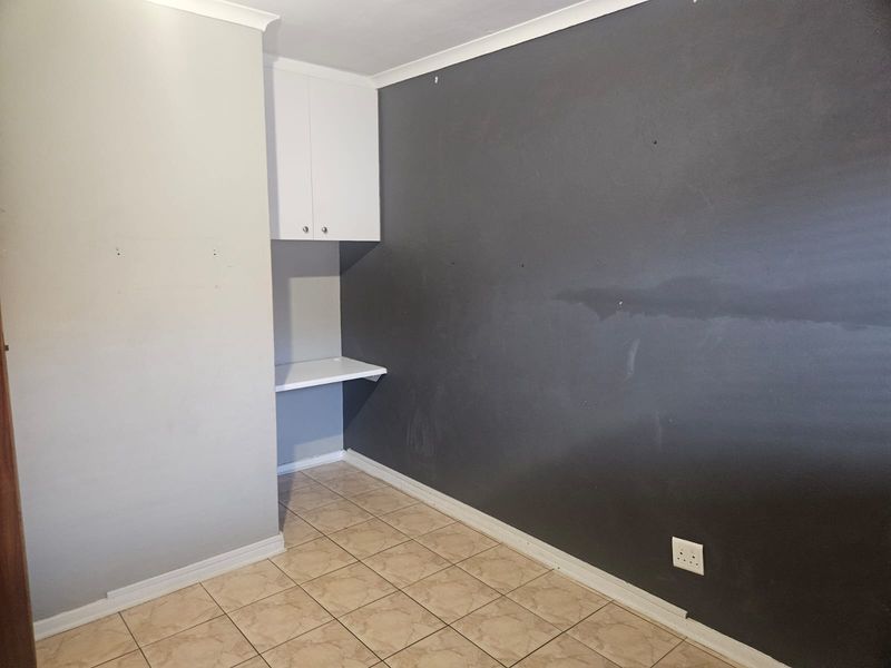 A small office space featuring tiled flooring, a built-in desk, and overhead cabinetry, currently requiring cosmetic wall repairs and repainting.