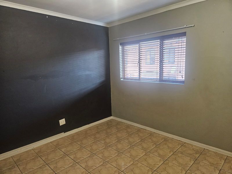 An empty bedroom featuring tiled flooring, a dark accent wall, and fitted venetian blinds, providing a neutral base for personalization.