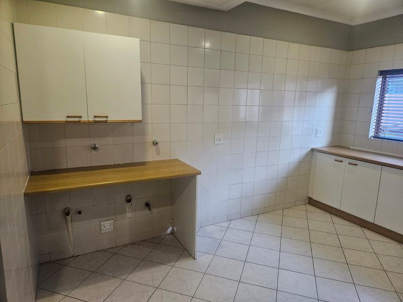 A functional laundry area featuring tiled walls and floors, built-in cabinetry with laminate countertops, and dedicated plumbing connections for appliances.
