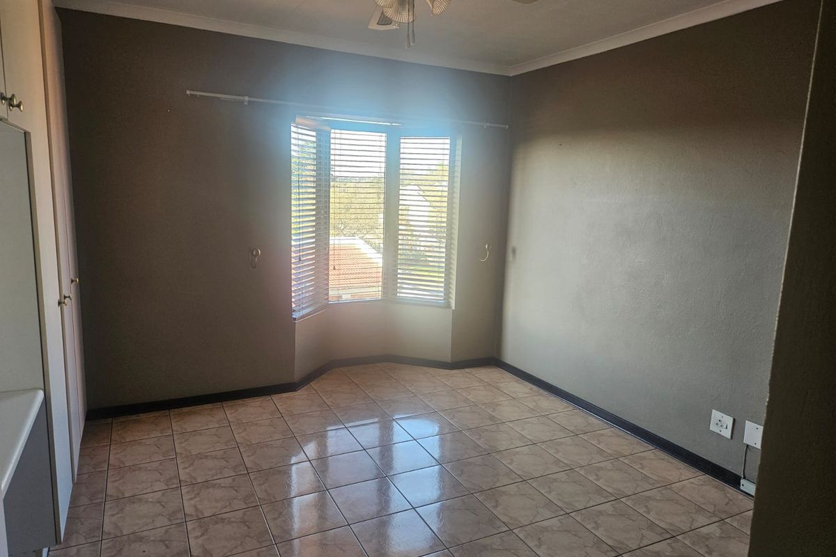 An empty bedroom featuring tiled flooring, a ceiling fan, and a bay window with fitted blinds, offering a neutral canvas for personalization.