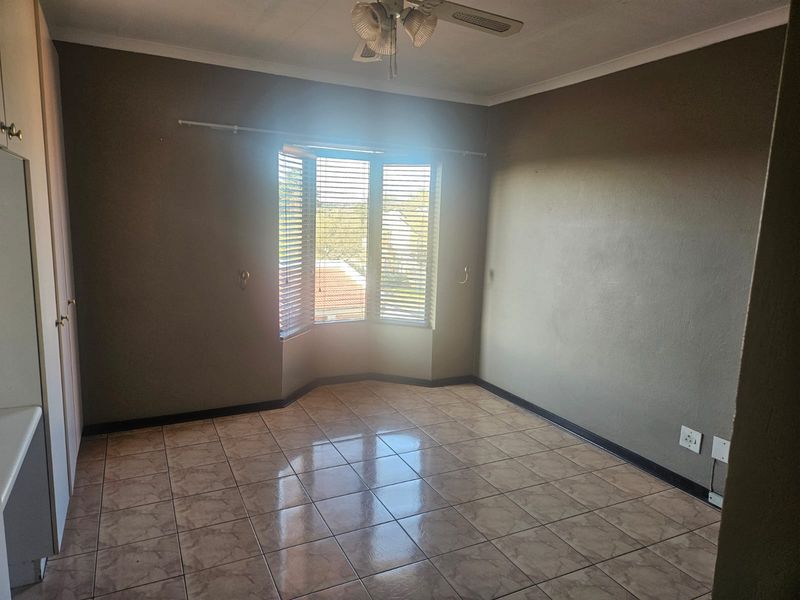 An empty bedroom featuring tiled flooring, a ceiling fan, and a bay window with fitted blinds, offering a neutral canvas for personalization.