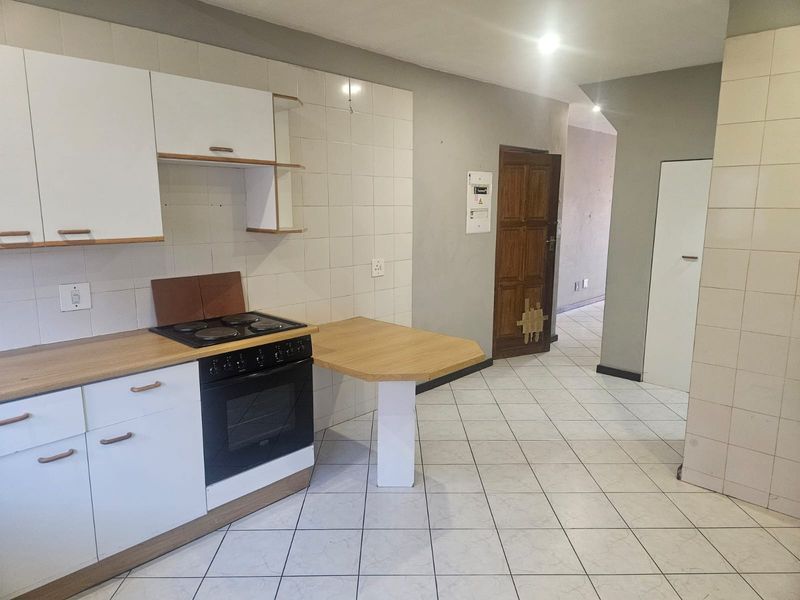 A functional kitchen featuring white cabinetry, a built-in electric stove and oven, tiled splashbacks, and a breakfast counter, with direct access to the hallway.