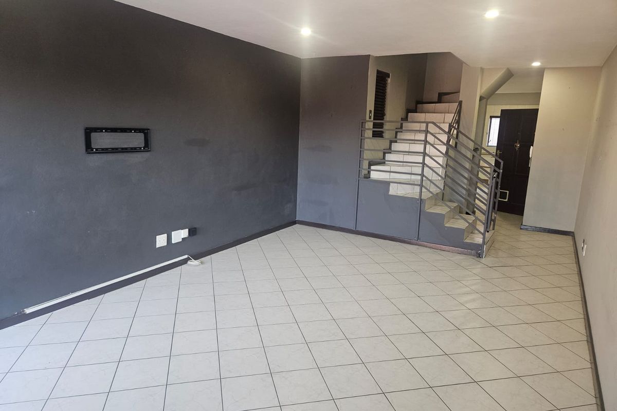 An empty living room featuring tiled flooring, a staircase with a metal railing, and dark accent walls, providing a blank canvas for interior design.