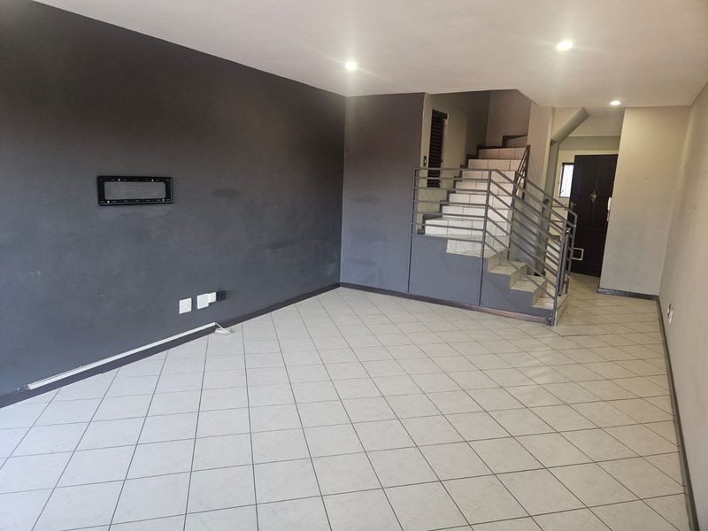 An empty living room featuring tiled flooring, a staircase with a metal railing, and dark accent walls, providing a blank canvas for interior design.