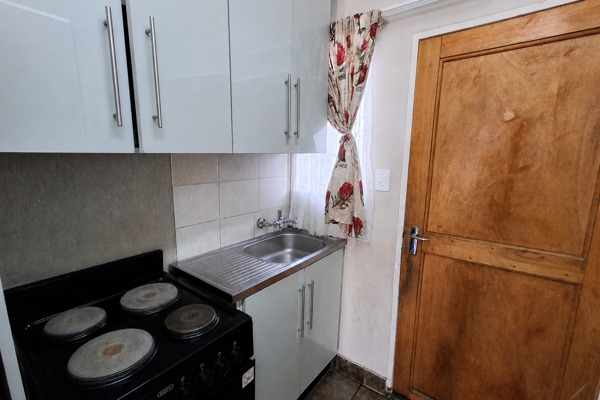 Compact kitchen area featuring white cabinetry, a stainless steel sink, and an electric stove, adjacent to a wooden door.
