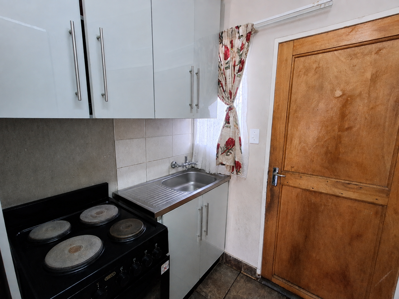 Compact kitchen area featuring white cabinetry, a stainless steel sink, and an electric stove, adjacent to a wooden door.