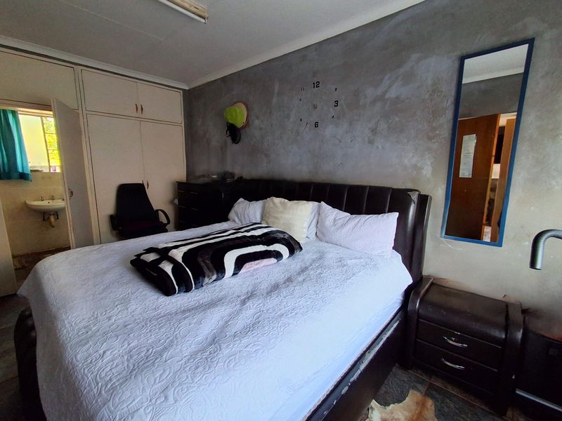 A bedroom featuring built-in cupboards, an en-suite basin area, and tiled flooring, with a textured feature wall.