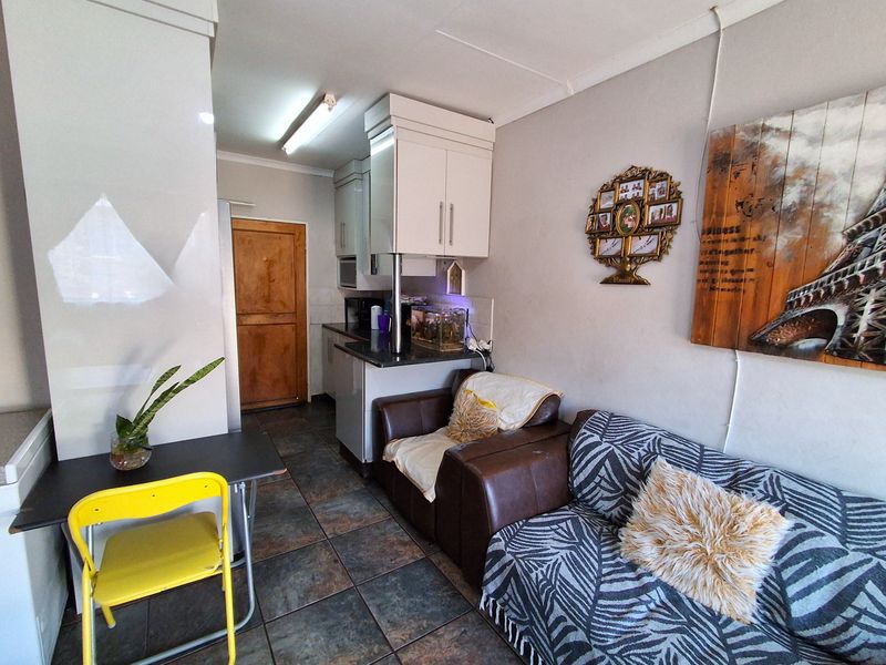Open-plan living area featuring tiled flooring, a compact kitchen with built-in cabinetry, and direct access to a timber door.