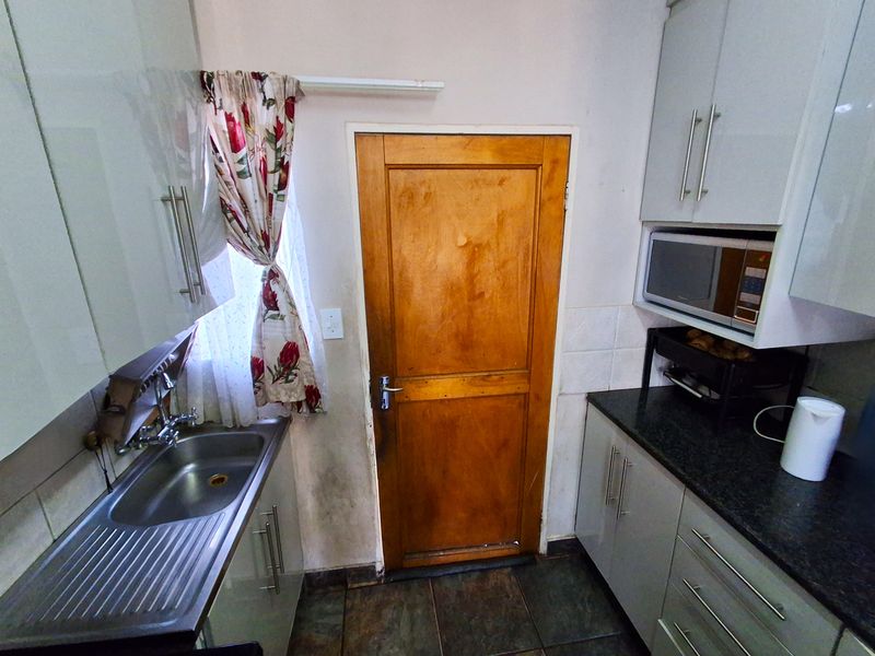 Compact kitchen featuring modern grey cabinetry, granite countertops, stainless steel sink, and a built-in microwave, with direct access via a wooden door.