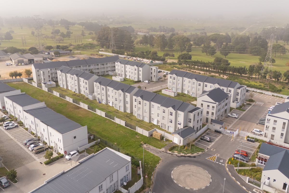 Aerial view of a modern apartment complex featuring multiple residential blocks, paved parking areas, and surrounding landscaped grounds.