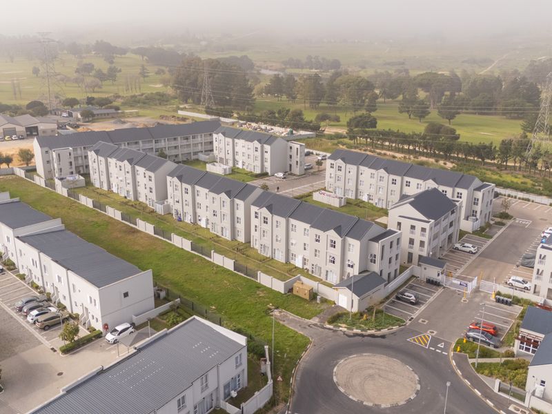 Aerial view of a modern apartment complex featuring multiple residential blocks, paved parking areas, and surrounding landscaped grounds.