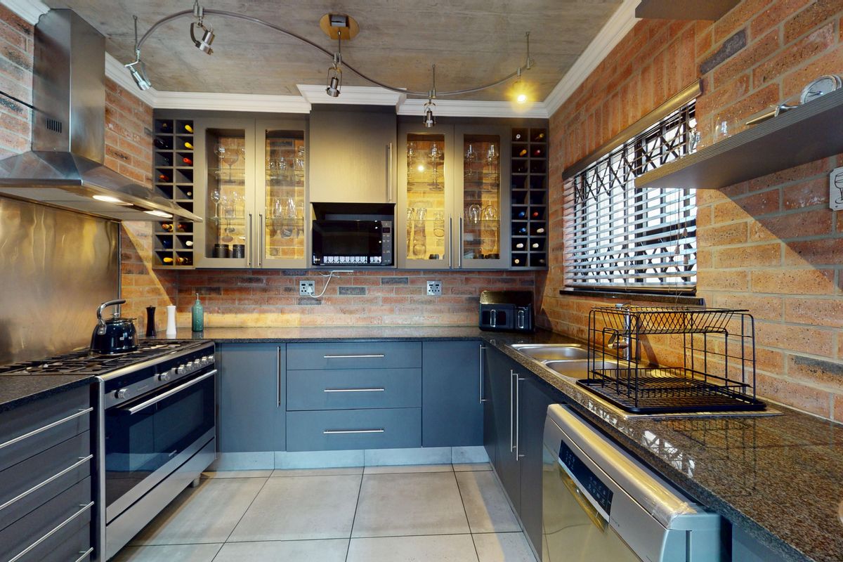 Modern industrial-style kitchen featuring exposed brick walls, concrete ceiling, granite countertops, and high-quality stainless steel appliances with integrated wine storage.