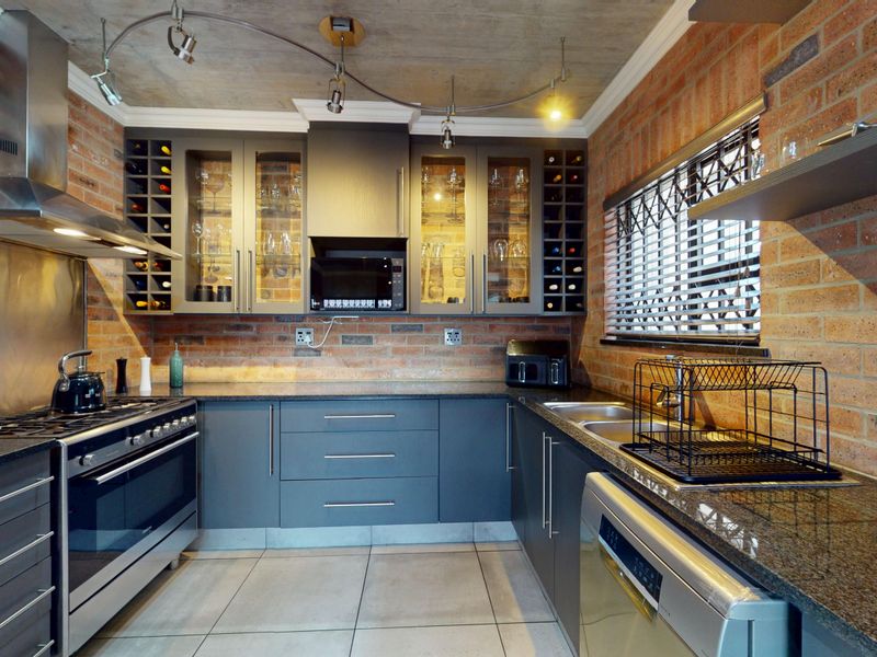 Modern industrial-style kitchen featuring exposed brick walls, concrete ceiling, granite countertops, and high-quality stainless steel appliances with integrated wine storage.