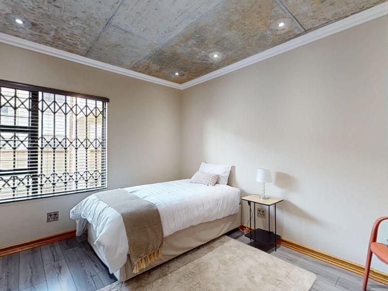 A bedroom featuring an exposed concrete ceiling with recessed lighting, laminate flooring, and a window fitted with a security gate.