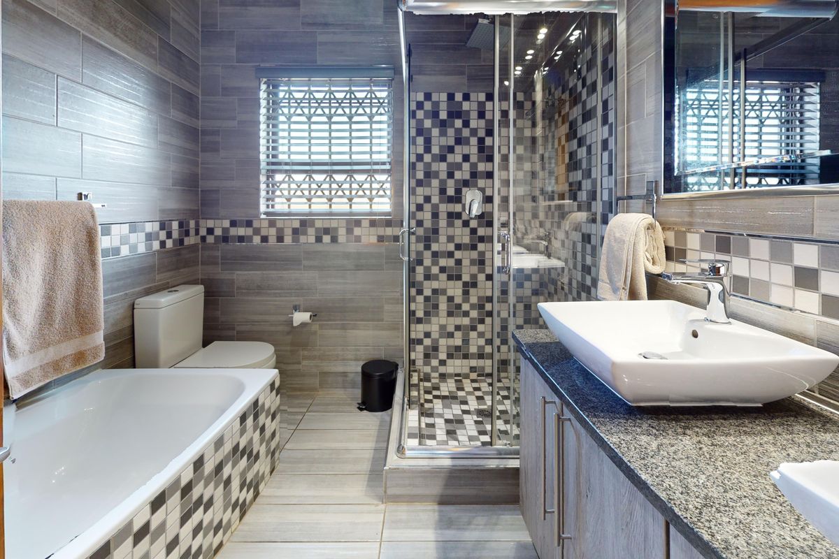Modern bathroom featuring a glass-enclosed shower, separate bathtub, granite-topped vanity with vessel sink, and contemporary grey tiled finishes throughout.