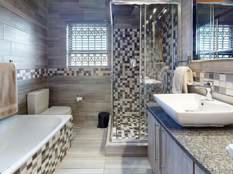Modern bathroom featuring a glass-enclosed shower, separate bathtub, granite-topped vanity with vessel sink, and contemporary grey tiled finishes throughout.