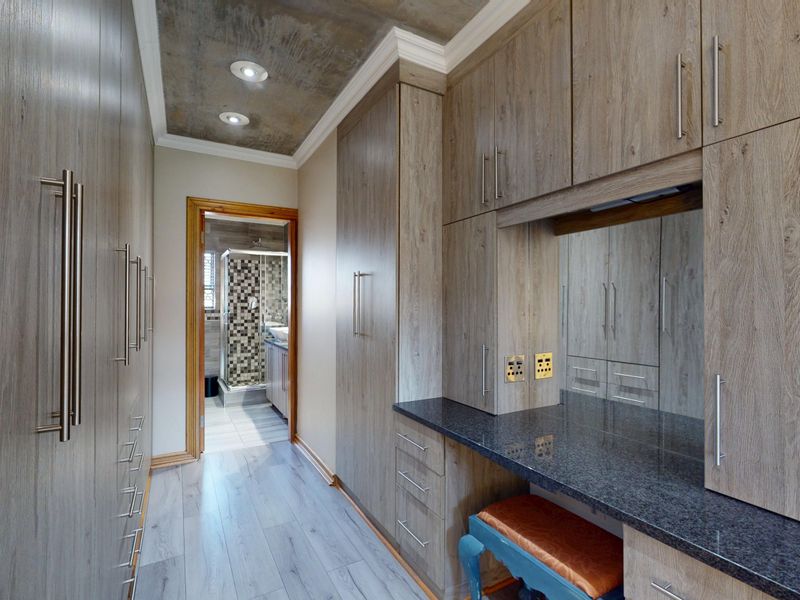 A modern dressing room featuring extensive built-in cabinetry, a granite-topped vanity area, and recessed lighting, leading directly into an en-suite bathroom.