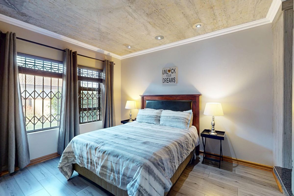 A well-maintained bedroom featuring laminate flooring, recessed ceiling lighting, and security bars on the windows.