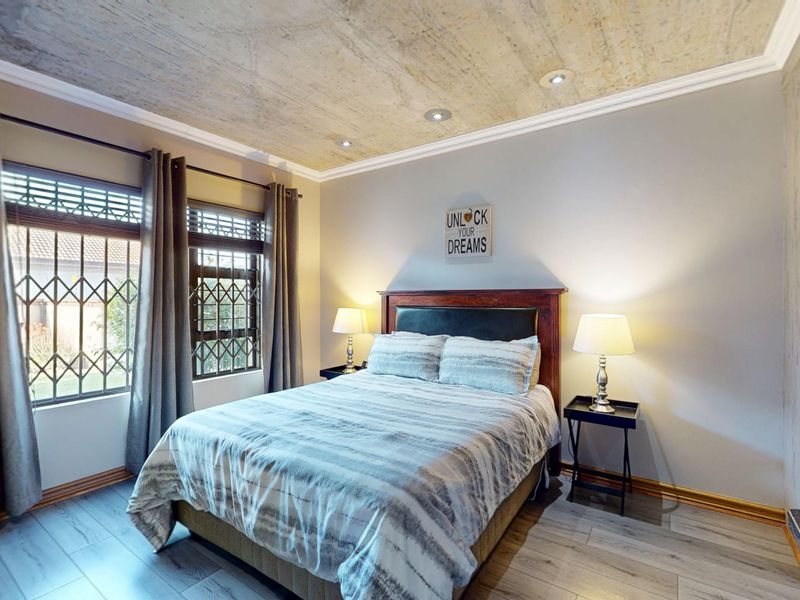 A well-maintained bedroom featuring laminate flooring, recessed ceiling lighting, and security bars on the windows.