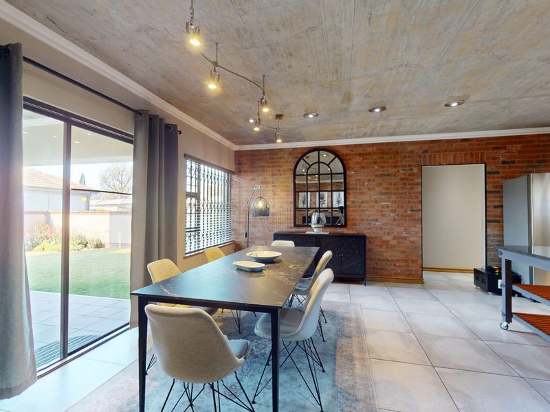 Spacious open-plan dining area featuring an exposed concrete ceiling, industrial-style brick wall, and large sliding doors providing seamless access to the outdoor patio.