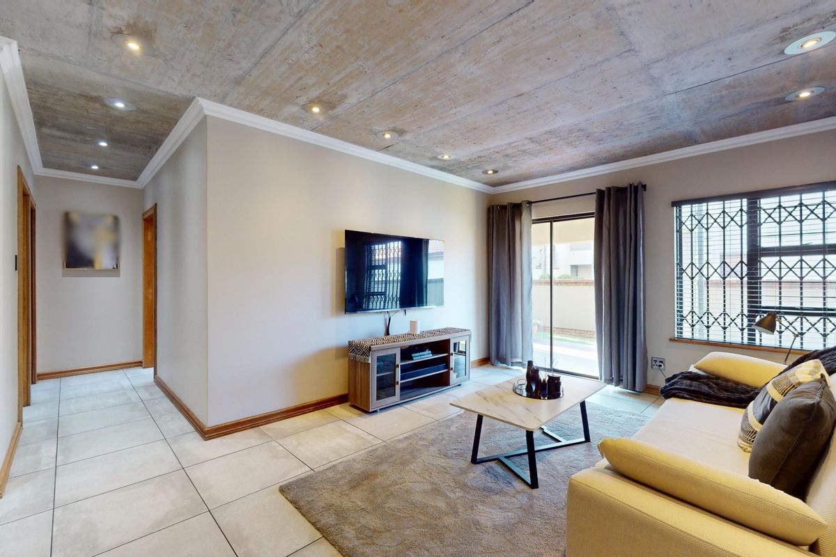 Modern living room featuring an exposed concrete ceiling, tiled floors, a brick feature wall, and direct access to an outdoor area via sliding doors.