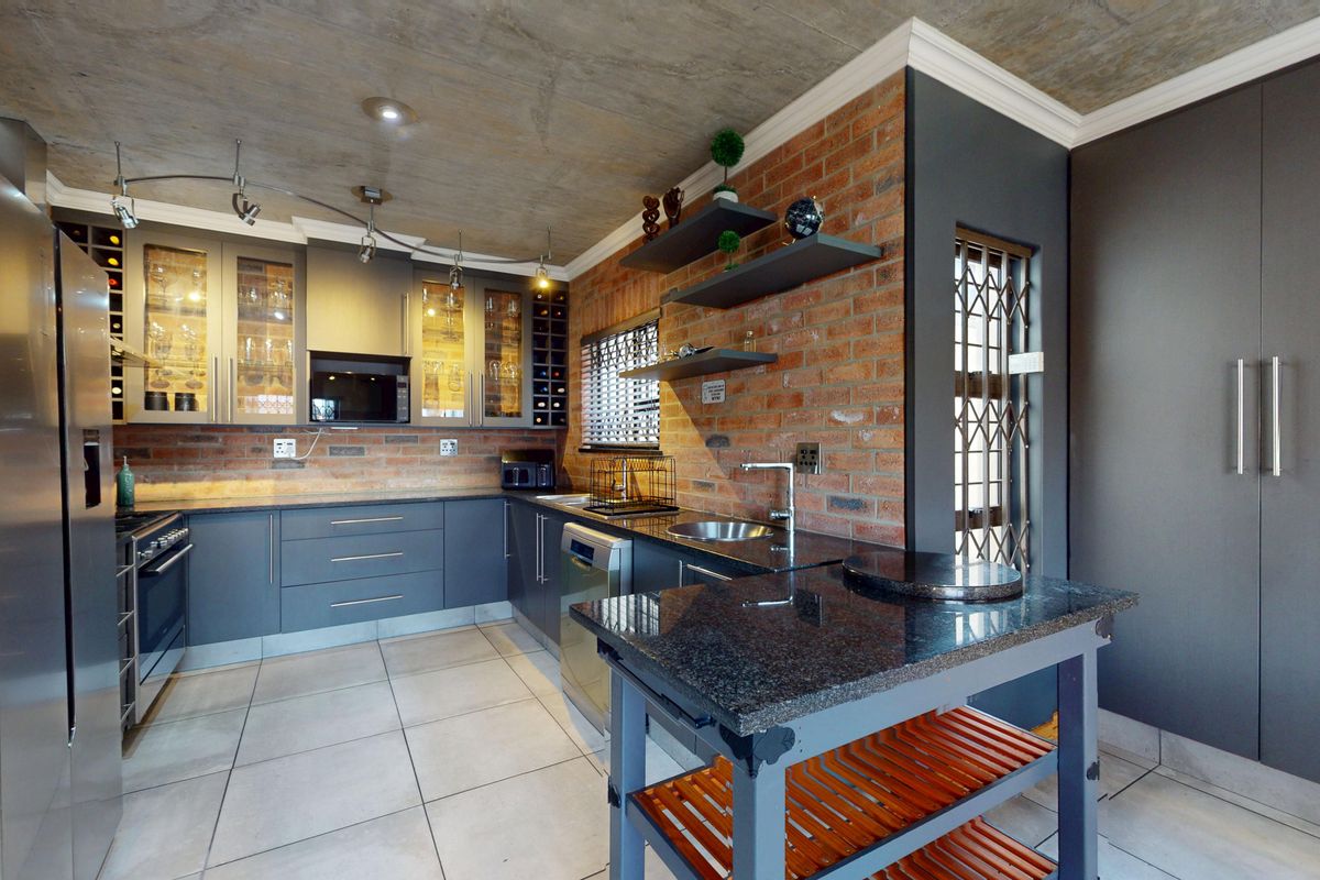 Modern kitchen featuring exposed brick walls, concrete ceiling, granite countertops, and ample built-in cabinetry with integrated appliances.