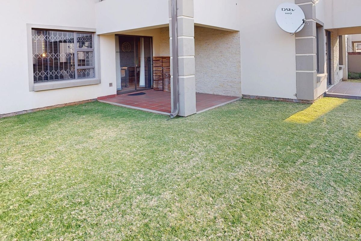 A well-maintained rear garden featuring a paved patio area, stone cladding accents, and secure window bars on the building facade.