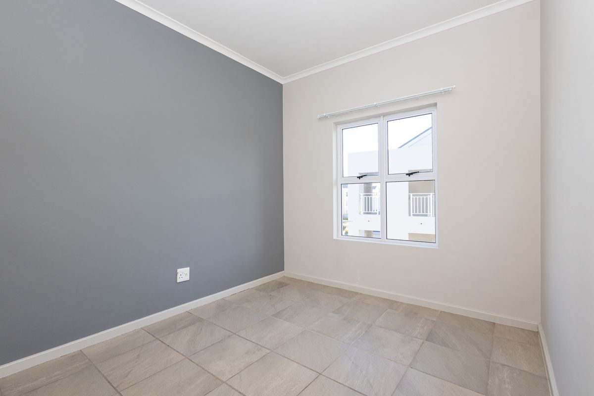 A clean, empty bedroom featuring neutral-toned walls, a grey accent wall, tiled flooring, and a window with a fitted curtain rod.