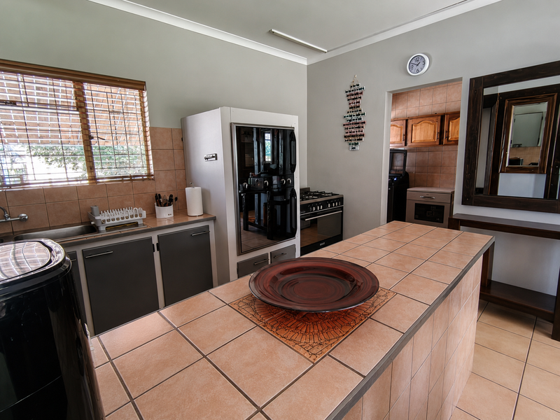 A functional kitchen featuring a tiled island, built-in oven, gas hob, and ample cabinetry, with an adjacent scullery area visible through the doorway.