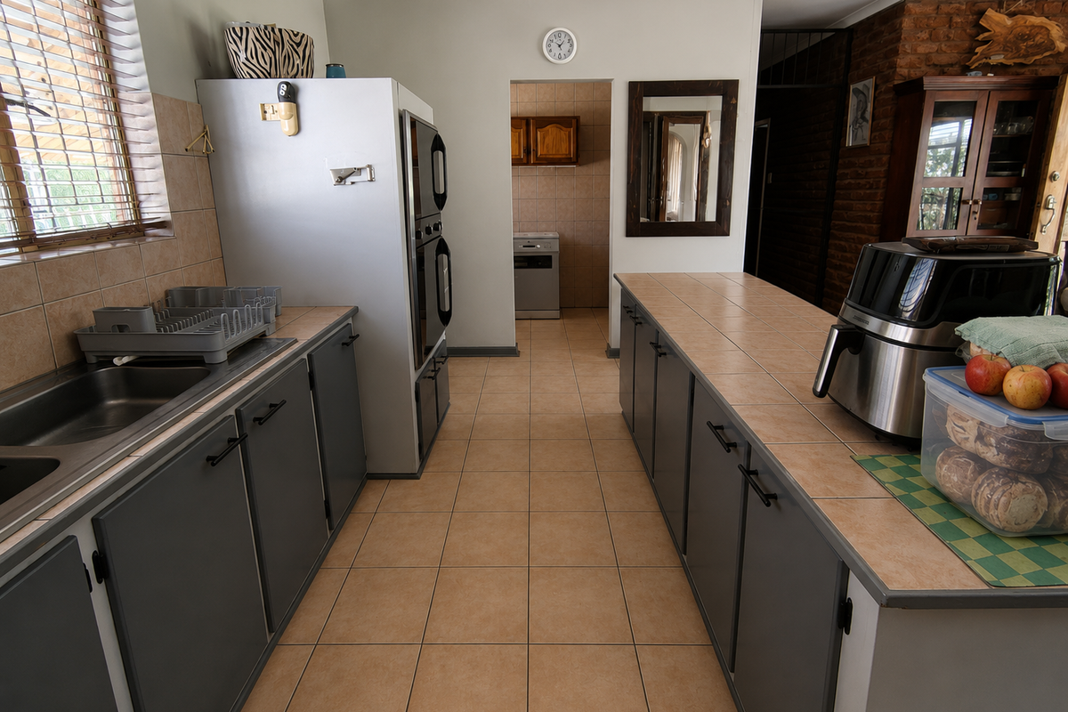 A functional kitchen featuring tiled countertops, built-in double oven, and ample cabinetry, with a scullery area visible through the doorway.