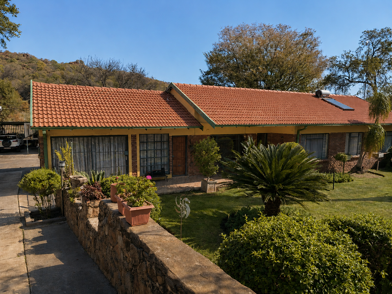 Front view of a single-story house featuring a terracotta tiled roof, solar water heating system, brick exterior, and a landscaped front garden.